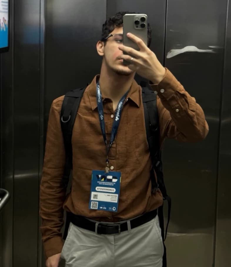 Gustavo Queiroz de camisa marrom e crachá de congresso, numa selfie no espelho do elevador.